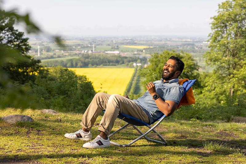 En man sitter och skrattar i en solstol i en skogsglänta. 