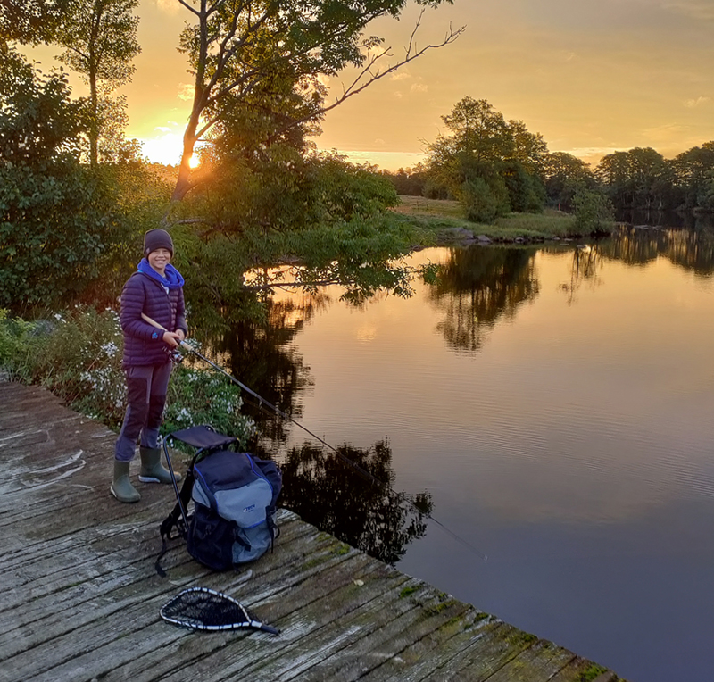 En ung kille står på en bro vid Lagan med ett fiskespö. Solen går upp. 