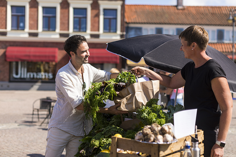 En man handlar grönskar på en marknad i centrala Laholm. 
