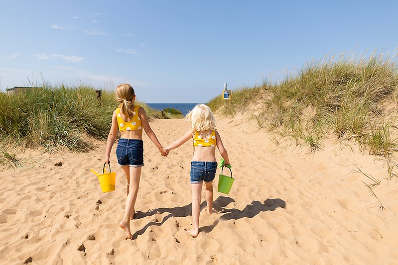 Två flickor håller handen på väg mot stranden och havet. 